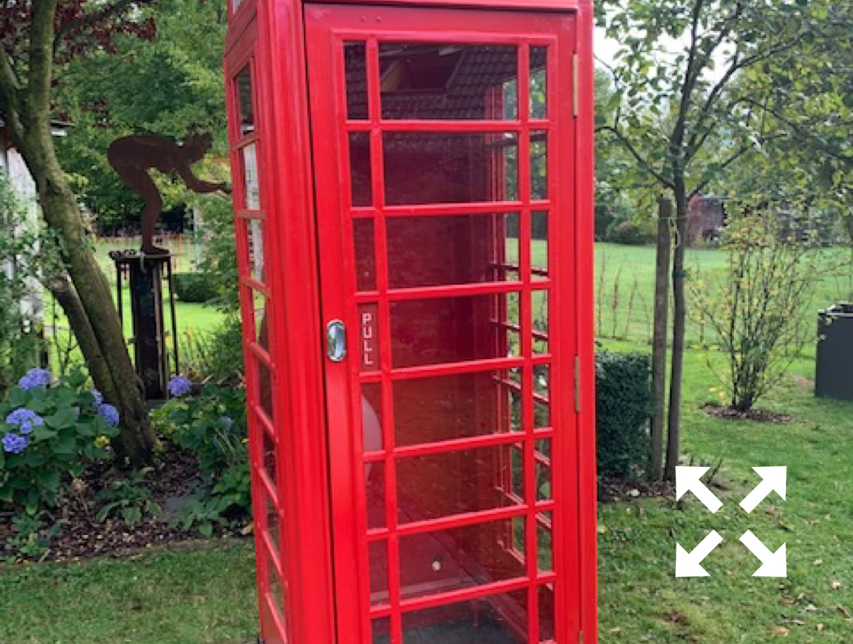 Eine rote K6 Telefonzelle steht in einem grünen Garten