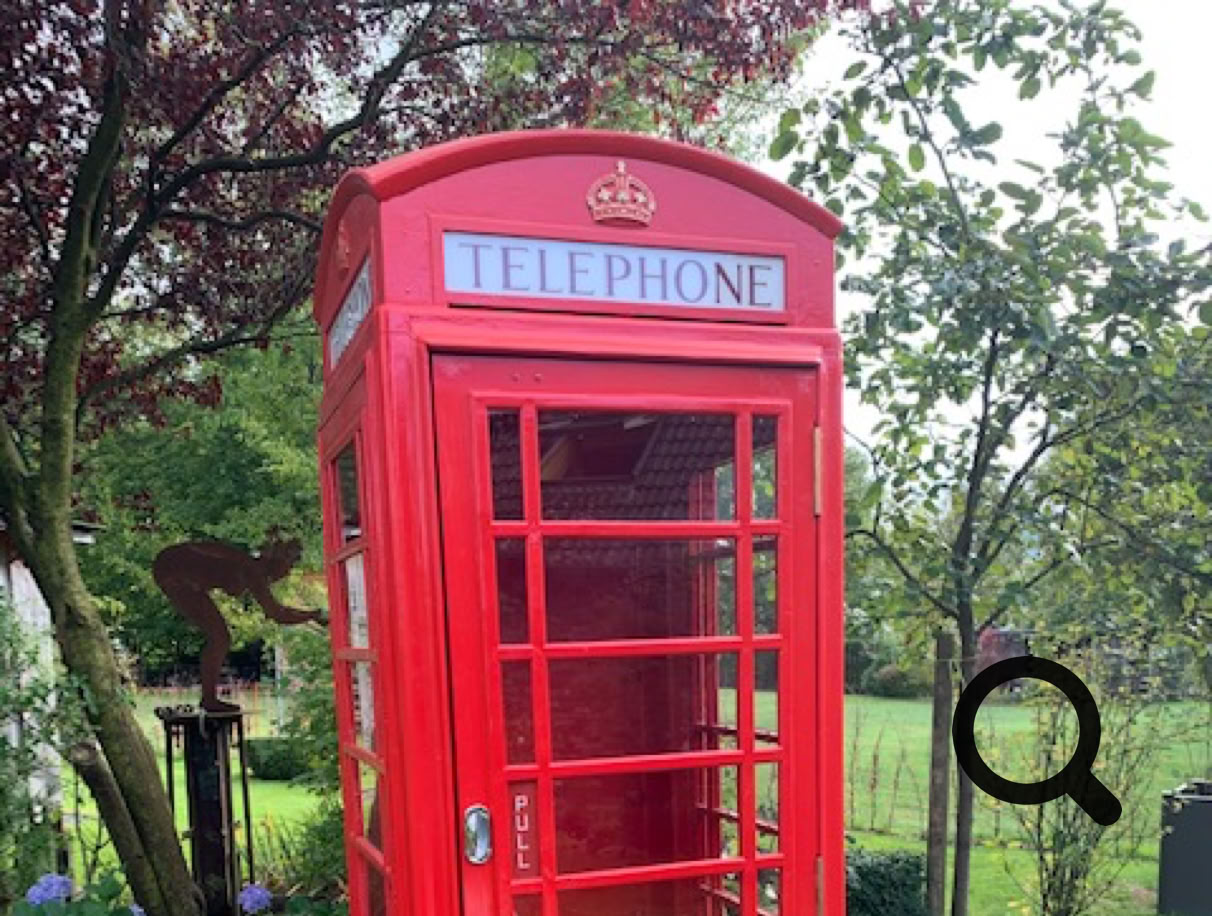 Eine rote K6 Telefonzelle steht in einem grünen Garten