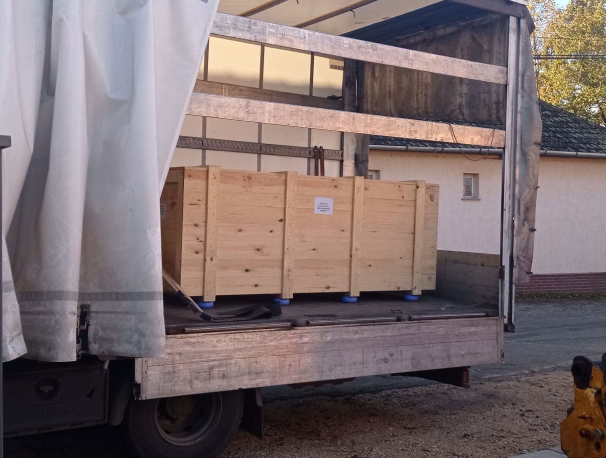 Ein geöffneter LKW mit einer Telefonzelle, die in einer großen Holzkiste auf der Ladefläche steht.