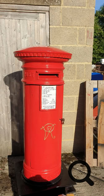Roter V.R. Briefkasten vor einer Steinmauer und Holztür.