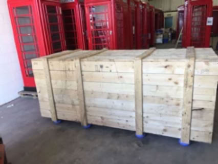 Holzkiste auf einem Boden, im Hintergrund mehrere rote Telefonzellen.