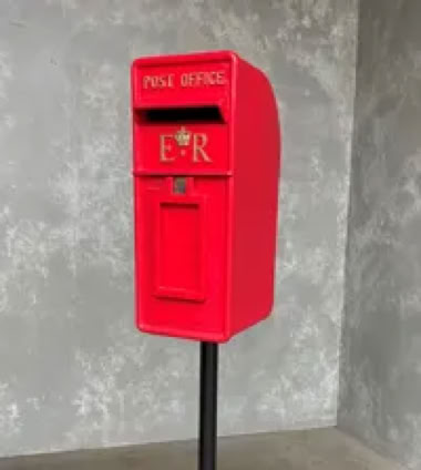 Roter Briefkasten auf einem schwarzen Ständer vor einer grauen Wand.
